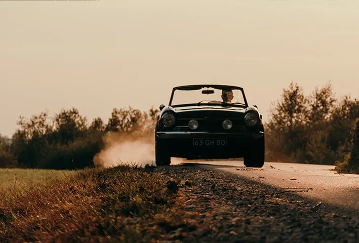 voorkant van oldtimer cabrio rijdend op weg met stuivend zand