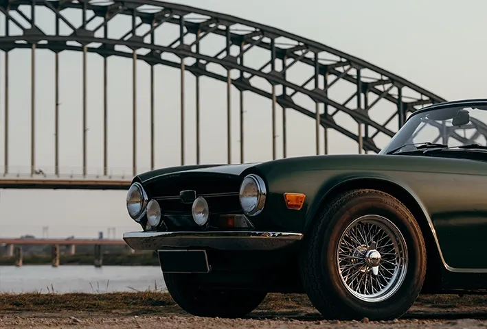 foto van een deel van de voorkant van een oldtimer met in de achtergrond een brug